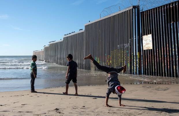Three boys, one mid-cartwheel, play next to the US-Mexico border fence in Playas de Tijuana, Baja California State, Mexico, on Dec. 29, 2018. Photo by Guillermo Arias, AFP/Getty Images
